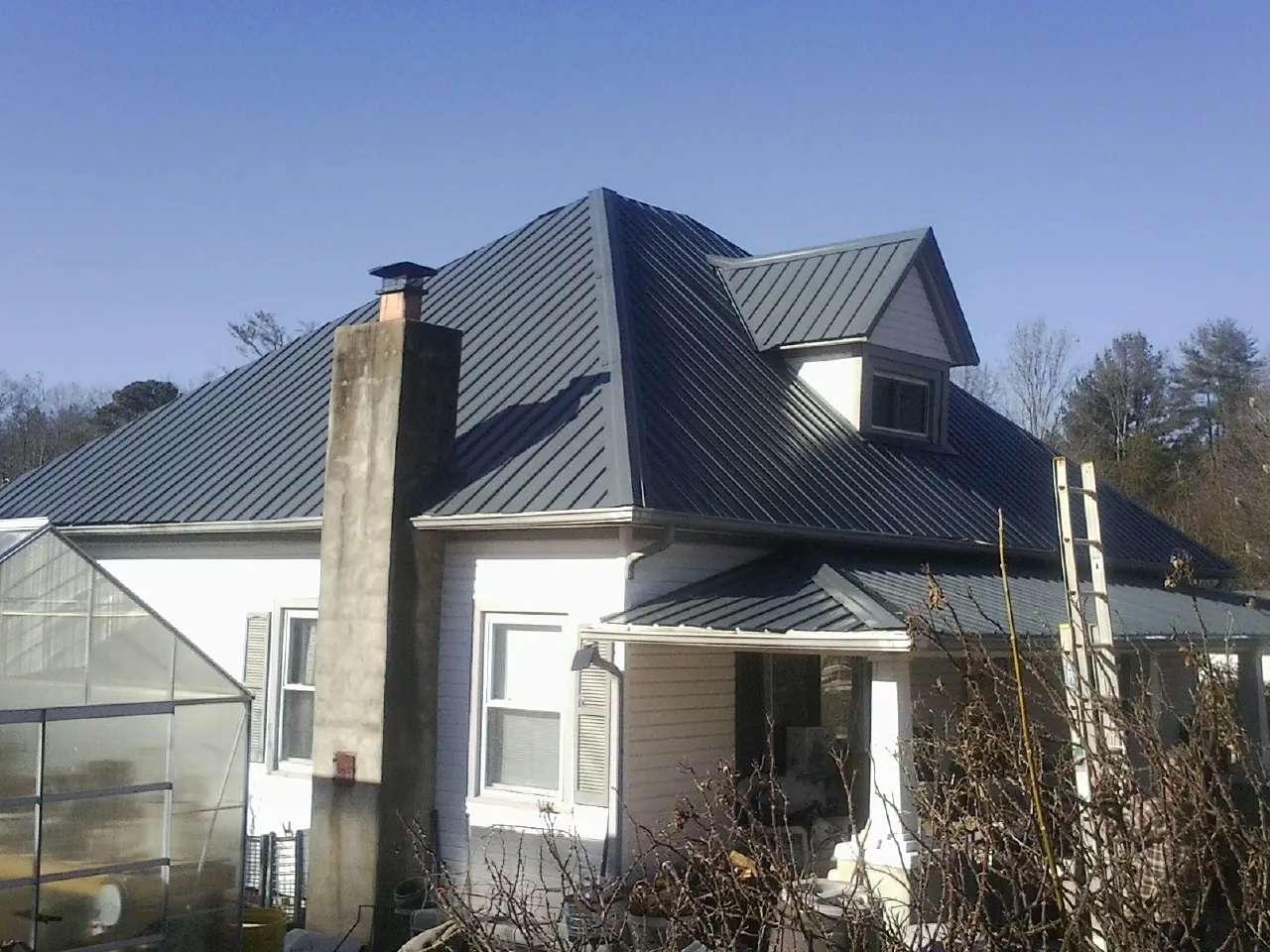 Dark blue standing seam metal roof on a white farmhouse with dormer — Slate & Tile Roof Repair by Roofing Brothers in Trafford