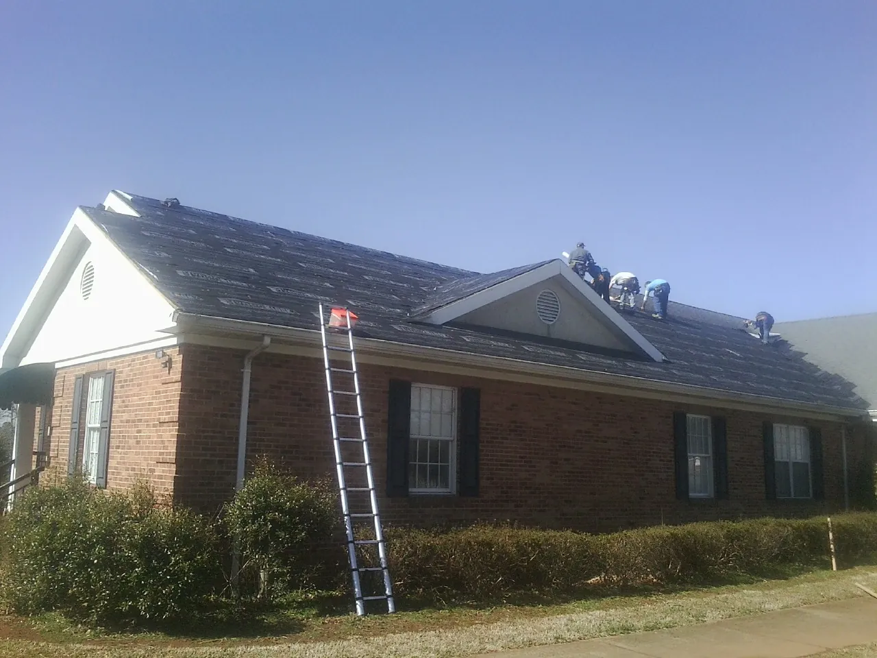 Crew tearing shingles off a brick ranch roof with a ladder set — Emergency Roof Repair work by our crew in Trafford