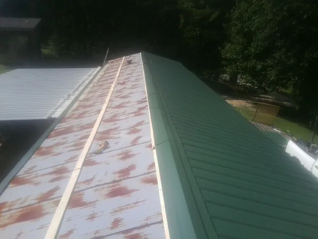 Old rusted panels beside newly installed green metal roofing — Wind Damage Roof Repair by Roofing Brothers in Trafford