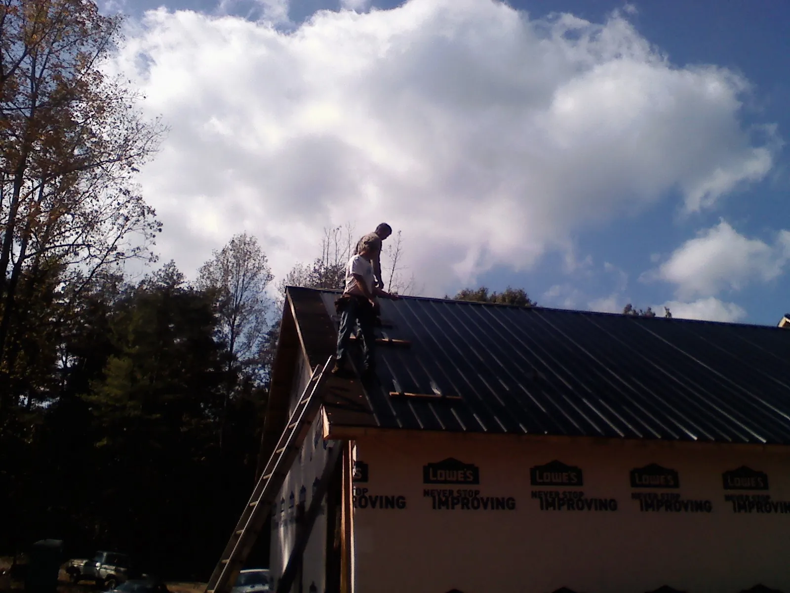 Roofer fastening dark metal panels high against a cloudy sky, from a Roof Inspection job in Trafford